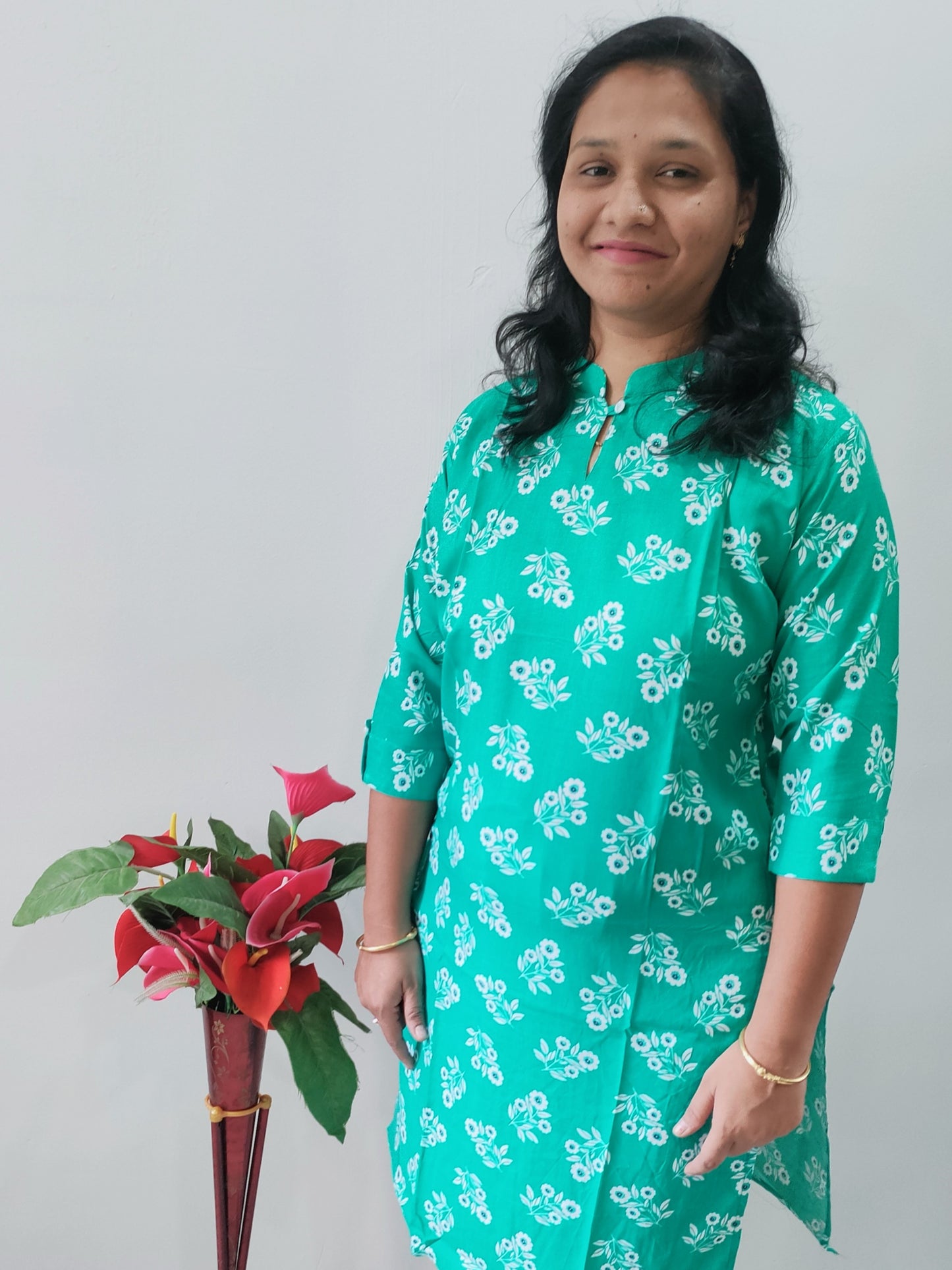 Woman wearing a premium rayon kurti with pocket in green floral print, posing next to a plant