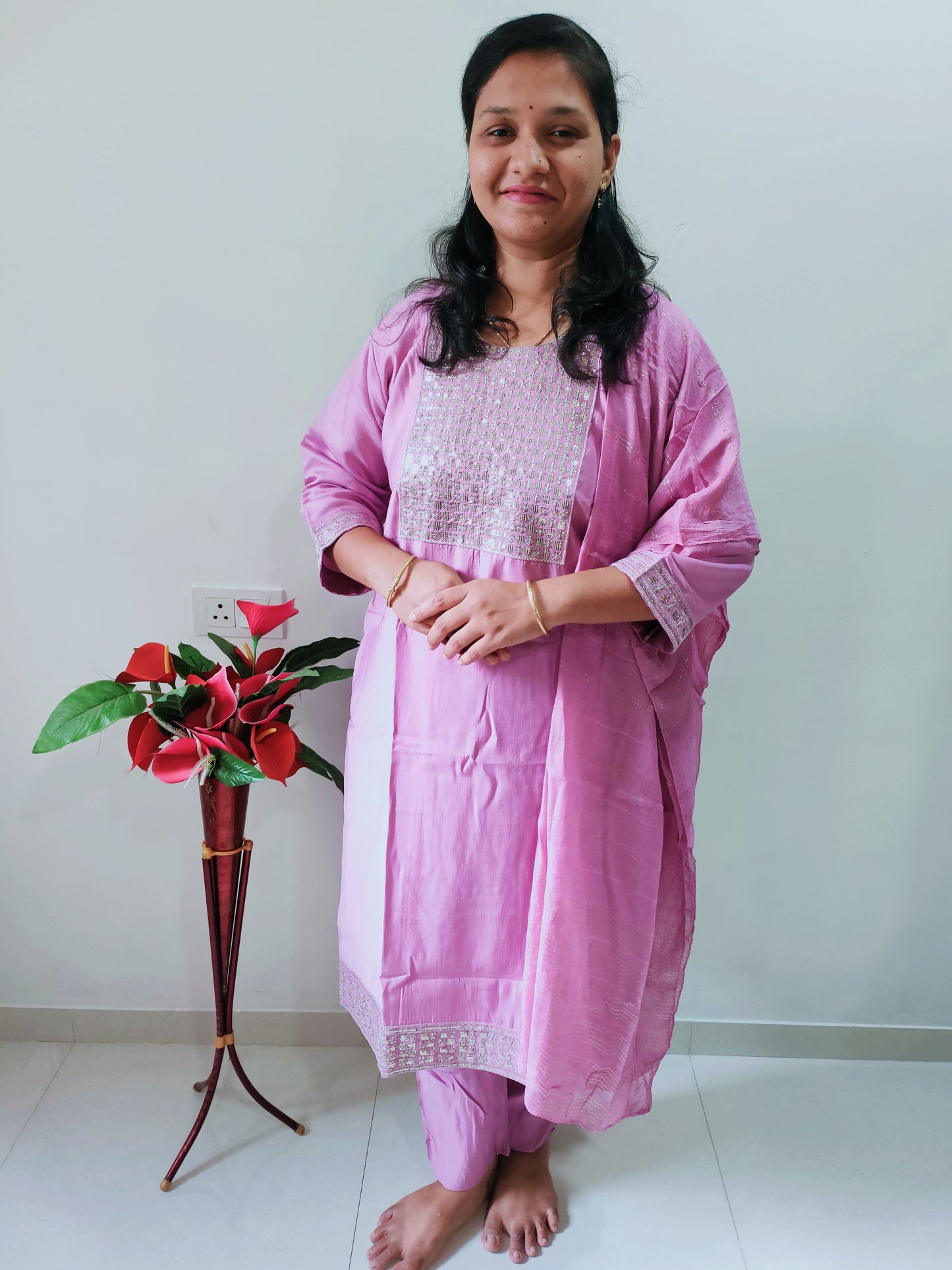Elegant woman in a pink Premium Silk Kurti Set standing beside a decorative plant
