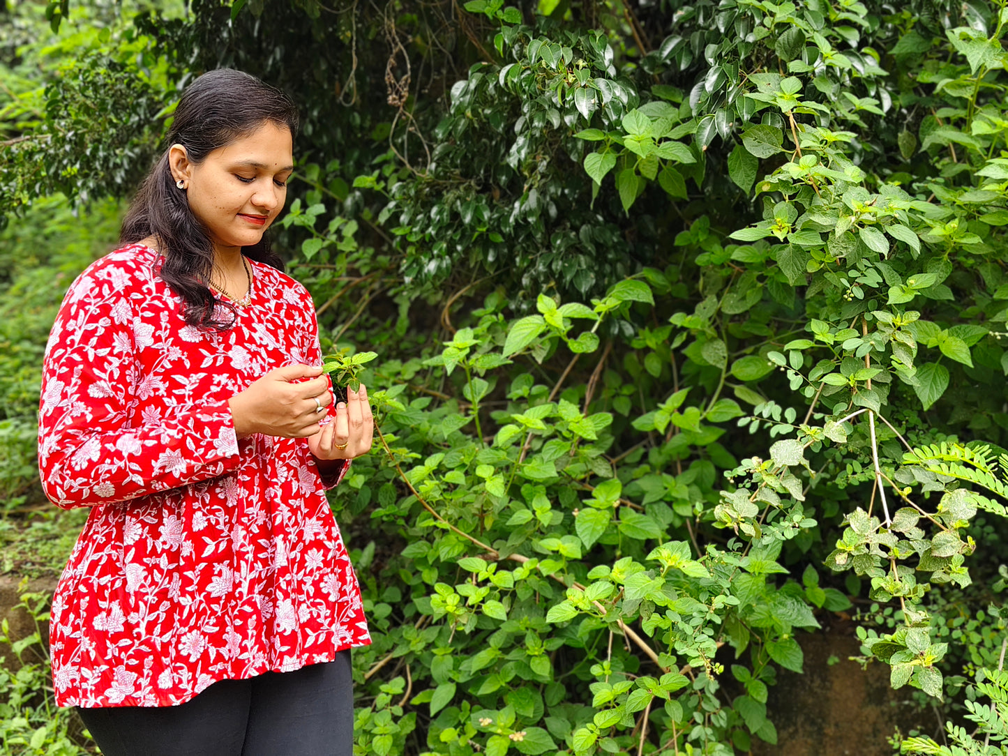 Elegant red peplum top for women with floral print, styled in a natural outdoor setting