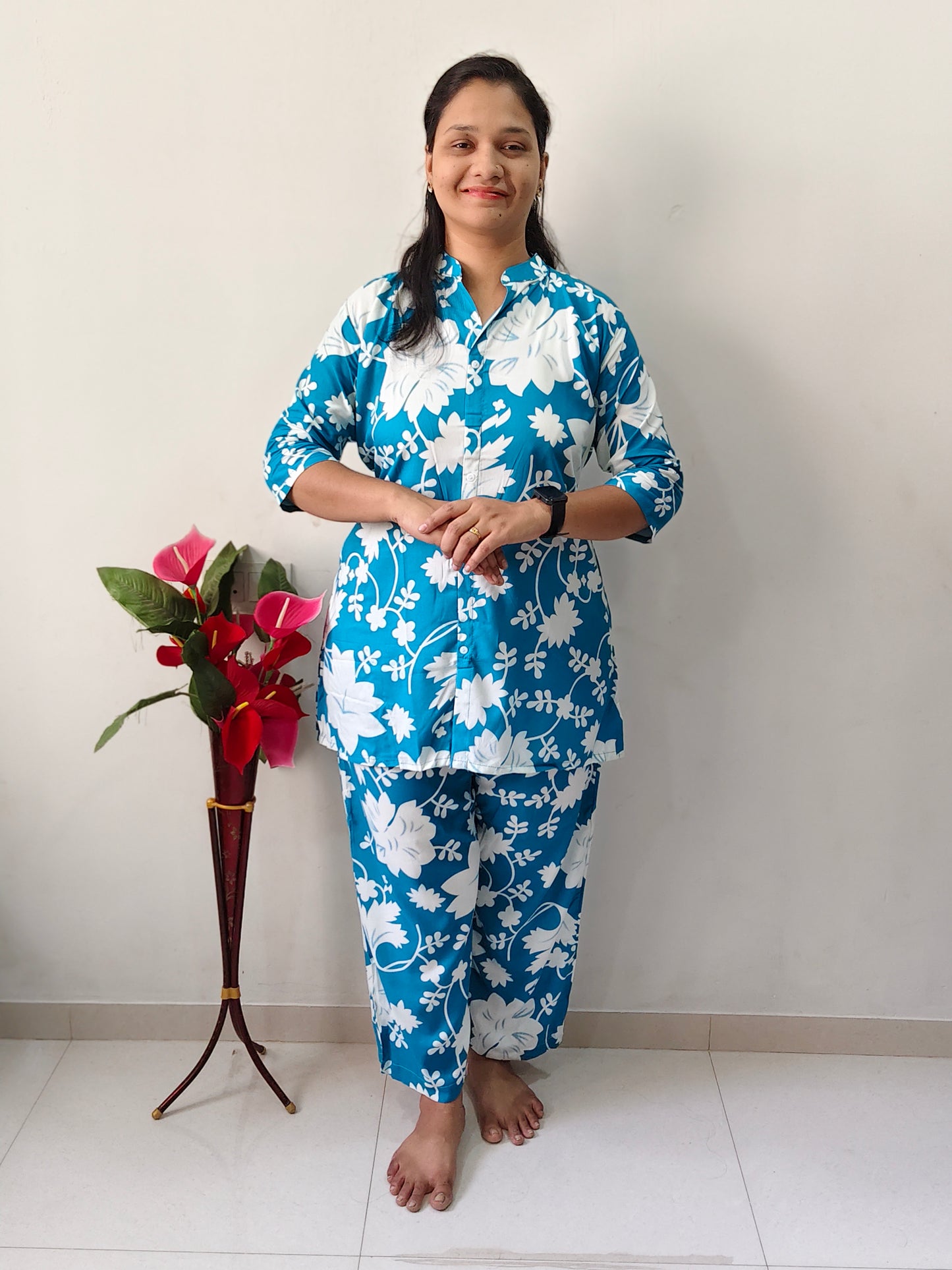 Woman wearing a sky blue cord set featuring white floral patterns, standing beside a flower vase
