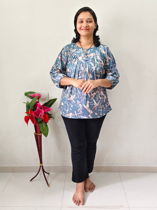 Woman wearing a fancy pleated top for women in blue floral design paired with black pants indoors